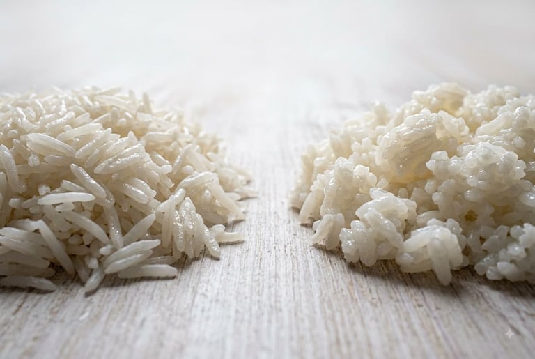 Two mounds of cooked white rice on a pale wooden surface — long, slender, separate basmati grains on the left, and shorter, plumper jasmine grains clinging together on the right