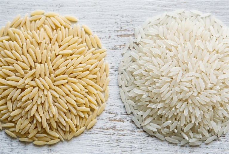 A round heap of pale yellow dry orzo beside a heap of white long-grain rice on whitewashed wood, shot from overhead so the blunt-ended pasta and the pointed translucent grains are both visible