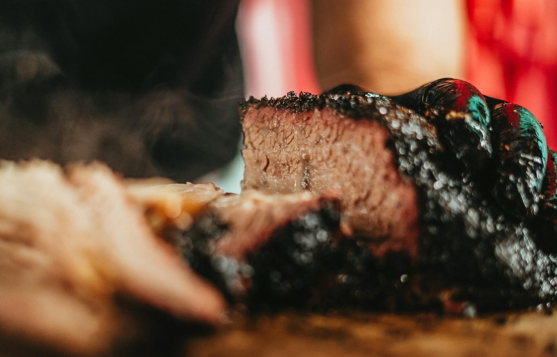 Tender Beef Brisket sliced on a wooden board with smoke rising, rich bark crust